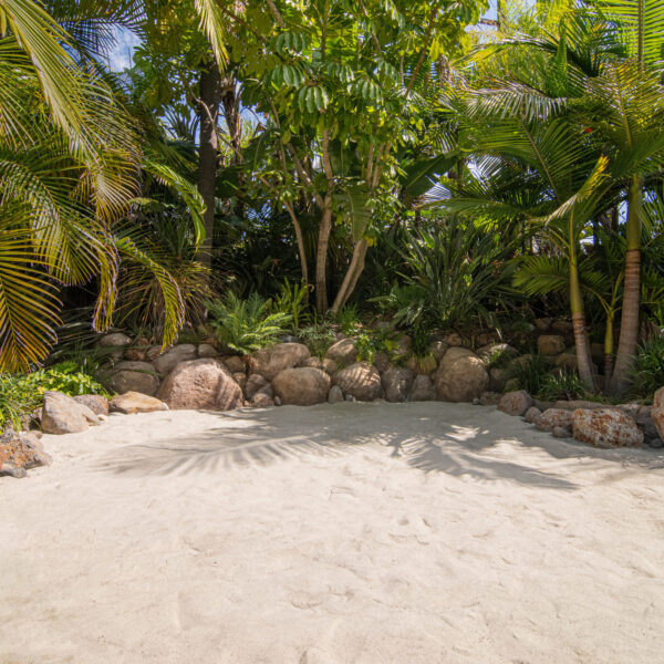 Empty white sand beach with lava rock Boulders and dense jungle foliage in background at Tropic Shots production set
