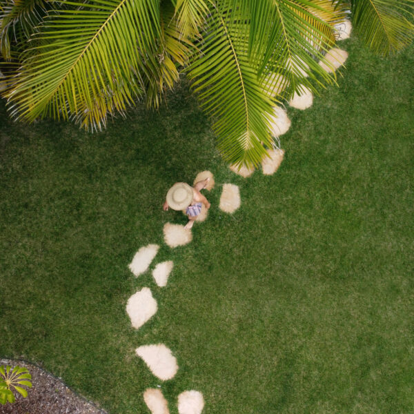 Top down view of model walking along Flagstone walking path through grass with palms overhanging at Tropic Shots production set