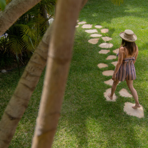 Model stepping along walking path through grass toward beach at Tropic Shots production set